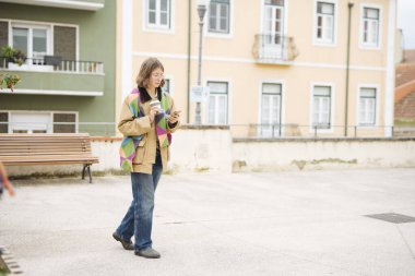 Sokakta yürüyen genç bir kadın telefon ve bildirimi kontrol ediyor, hareketli tempo ve gelişigüzel katmanlar, kentsel cepheler ve tramvay hatları