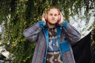 Kulaklıkları yakın portrede ayarlayan adam, derin bakışlar ve kulaklıklarda eller, desenli ceket ayrıntıları, samimi duyusal anlar.