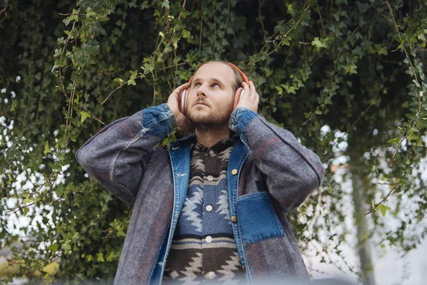 Kulaklık takan adam, sallanan yaprakların altında, gözleri kapalı ve elleri kulaklarda, rahatlamış açık havada dinleme anı