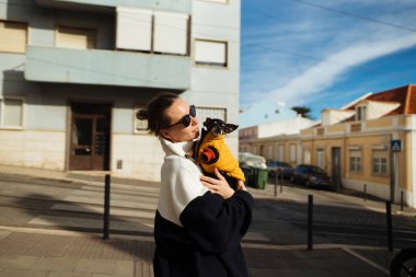 Evin yanında küçük bir köpek beşiği, sarı duvar arkaplanı, nazikçe sarılmak, yüzüne tünemiş güneş gözlükleri, motosiklet silueti,