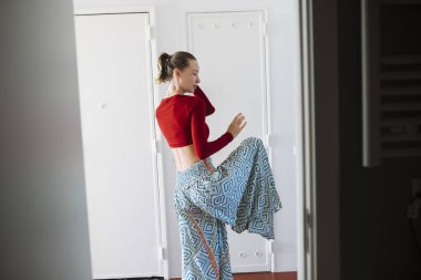 Performans sanatçısı bir bacağının üzerinde desenli etek, dengeli duruş ve merkezli hizalama, sessiz eğitim anı ile eşikte duruyor.,