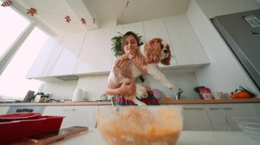 Kadın spanyeli kaldırırken karıştırma kabının üzerine sırıtıyor, cam kasede görünen hamur parçaları, parlak mutfak penceresi, sıradan ekose.