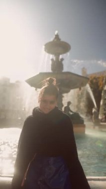 Güneşli çeşme portresi beyaz kadın, şehir meydanına yansıyan düşünceli öğrenci, yumuşak çörek ve örgü süveter, nazik lens.