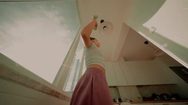 Geniş açılı gündoğumu kaldırışı, açık pencerenin yanında kadın görüntüsü, tek bir dambıl kaldırışı, sıcak ışık, çatı katı tarzı daire.,