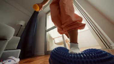 Aydınlatılmış pencerenin yanındaki mavi yastığın üzerinde dengelenmiş ayaklar, çoraplarla oynak denge çalışması ve tahta üzerinde dikenli masaj topu.