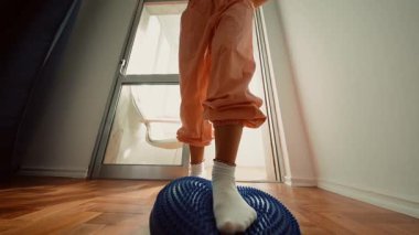 Sabah provası sırasında mavi denge diskine adım atan kişi, modern dansçı ayak hareketlerini ve duruşunu inceliyor