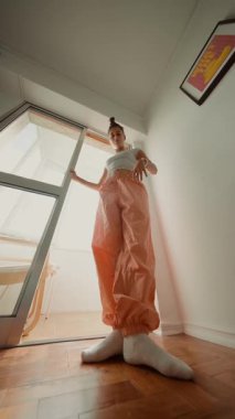 Düşük açılı editoryal poz oturumu turuncu pantolonlu ve beyaz bluzlu, sakin modellik yapan genç kadını sunar.