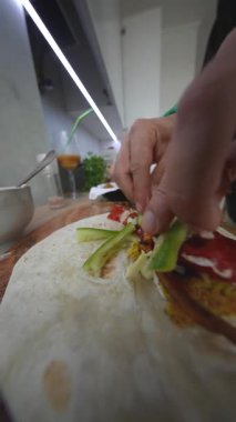 Tortilla 'yı renkli sebzelerle, kavrulmuş biberlerle, beyaz sokak usulü salatalıkla, kırmızı soğanla dolduran eller.