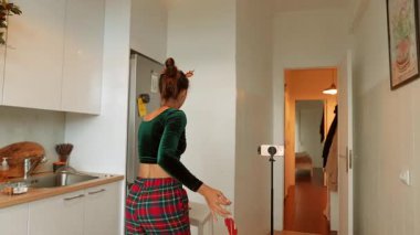 Beyaz kadın mutfak girişinde kırmızı çelenk düzenliyor, neşeli parti planlayıcısı şenlikli flamalar kuruyor, organize hazırlık yapıyor.