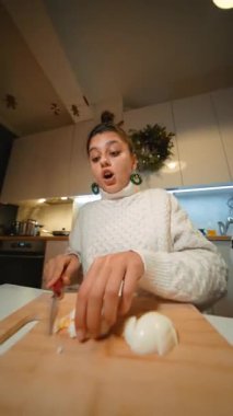 Mutfakta soğan doğrayan genç kadın süveter ve çörek, bıçak kayma anı, yakın çekim elleri