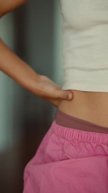 Elin kalçaya yakın duruşu, pembe pantolonlu parmak ucu bel hizasında, koyu renkli tırnaklar, kesilmiş beyaz kaburga üstü, elastik.