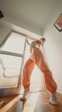 Beyaz sanatçı uzun pozlar veriyor güneş ışığında, geniş turuncu pantolonlar ve çoraplar, düşük kamera açısı boy ve özgüveni vurguluyor,