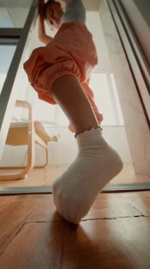 Lowangle parmak uçlarında yakın plan, kapıdaki ahşap zemin sürükleyici çoraplar, güneş ışığı vurgusu, turuncu koşucular, oyuncu dengeli hareket