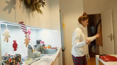 Beyaz kadın dekore edilmiş mutfakta fırın eldiveni, alet edevat ve paketlenmiş hediyelerle tezgah tutuyor.