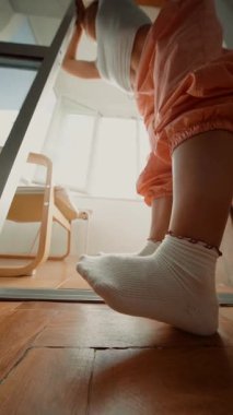 Kapı aralığı, beyaz çoraplar, ahşap zemin ve arka planda güneşli sandalye, turuncu koşucular, sakin bir ev varlığı.