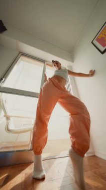 Yaratıcı beyaz yürüme sekansı açık pencerede, turuncu pantolonlar ve bilek çorapları güneş ışığını yakalıyor, ahşap üzerinde yavaşça yürüyor.