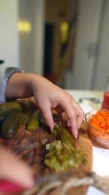 Yakınlarda doğranmış havuç, odaklanmış hazırlık çalışması, parlak mutfak ışığı ve kasıtlı olarak tahtadan turşu dilimleyen eller.