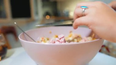 Beyaz kadın elleri ahşap tahtada ve pembe kasede malzemeleri doğruyor ve karıştırıyor. Turkuaz yüzük görünür, bıçak yakın plan.