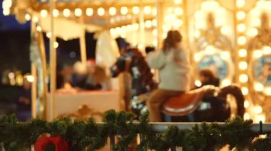 Alacakaranlık atlıkarınca ışıkları etrafını sarmış. Süslü atlarla ön planda şenlikli bir çelenk taşıyan bir grup arkadaş. Samimi, neşeli bir akşam.