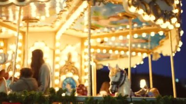 Çiftler akşam gökyüzünün altında yanan atlıkarıncayı izliyorlar, yumuşak altın ampuller ve siluetler, sıcak parıltılı samimi bir fuar yeri randevusu