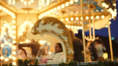 Akşam atlıkarınca ışıkları. Süslü atların üzerinde gülen bir grup arkadaş. Ön planda şenlikli bir çelenk.