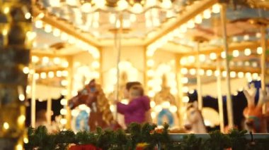 Kızlar sıcak ampullerin altında dönen atlıkarıncaya gülüyorlar, gece fuarı enerjisi, parıldayan süslemeler, samimi gülümsemeler ve rahat tatil havası.