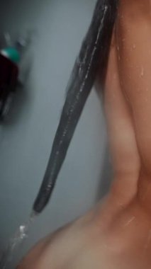 Islak saçlar ve çıplak omuz, şampuan köpüğünü gösteren yakın plan, ensedeki uzun koyu iplik üzerindeki su damlacıkları, saçları ayarlayan eller, yumuşak.