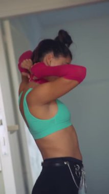 Kapının önündeki kadın süveterini çıkarıyor, turkuaz sutyen, kemerli siyah şort, pembe kol ısıtıcısı, sıradan bir apartman havası.