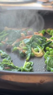 Tavada ıspanak ve bezelye cızırdıyor, spatula ev yemeğini mantarla pişirirken spatula tavadan buhar yükseliyor.,