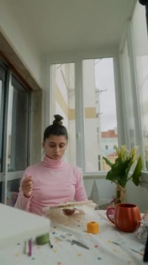 Beyaz kadın işlemeyi bitirmiş halkayı, güneşli masada zevkle inceliyor. Küçük bir kutlama jesti, temiz malzemeler.