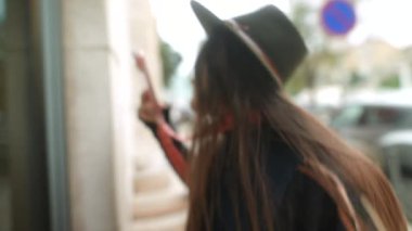 Şapka ile selamlama penceresi, cam yansıması, telefon açık, yumuşak hareket bulanıklığı, kaldırım taşı mağaza önü, sıcak tonlar, samimi