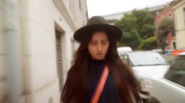 Şehrin kaldırımlarına saç atan neşeli kadın, canlı kafa hareketi, bohem şapka ve çapraz vücut torbası, neşeli enerji, samimi gülümseme.