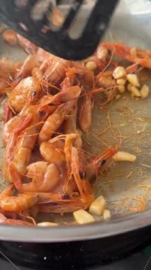 Tavada altın kavrulmuş karides, paslanmaz yüzeyde karamelize edilmiş sarımsak küpleri, kabuğa yapışmış karamelize parçacıklar, spatula kaldırma.