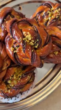 Kapalı tarçınlı çörekler gümüş tepside, haşhaş tohumları ve parlak jöleli ezilmiş şam fıstığı serpiştirilmiş, fırın tezgahı vitrininde