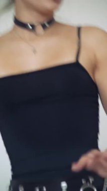 Zincirleme kemeri ve yırtık taytları ayarlayan kadın, siyah stüdyo kıyafetleri içinde elleri ve kalçaları, boğucu ve metal detaylarıyla yakın plan.,