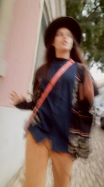 Şehir merkezindeki moda yürüyüşünde kaldırım taşı üzerinde katmanlı şapkalı bir kadın görülüyor. Sokak sanatçısı eski mimarinin hareketli adımlarını atıyor.,