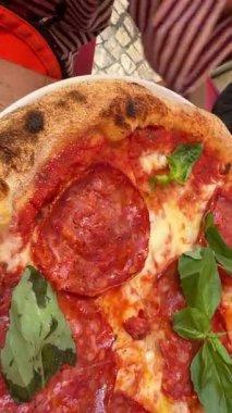 Yakın plan pepperonili pizza. Elleri kesilmiş, taze fesleğen ve kavrulmuş ekmek. Beyaz tabak üzerinde pembe bir sokak kahvesi anı.