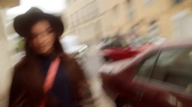 Dar şehir caddesini keşfeden mutlu bir kadın, hayat dolu bir yürüyüş, şapka ve çapraz vücut çantasıyla, parlak bir ifade ve neşeli adımlarla,