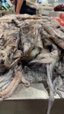 Pırıl pırıl derisi ve kıvrımlı manto, paslanmaz levha, satıcı hareketi ve kalabalık balık tezgahı atmosferine sahip buzdaki mürekkep balığı.