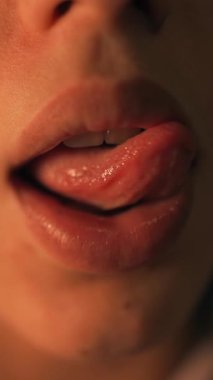 Kapalı ağızlı, karamsar turuncu ışık altında beyaz erkek, dil yuvarlamaları ve dudak gerginliği ile ses pratiği, cesur, samimi bir tarz.