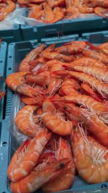 Portakal karidesleri sandıkların içinde canlı pazar vitrininde satıcı buzda taze balık yakalıyor parlak kabuklara odaklanıyor.