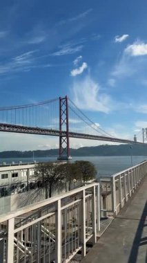 Kırmızı asma köprünün yanındaki rıhtım geçidi manzaralı, beyaz korkuluklu, uzun gölgeli, sakin