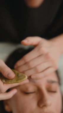 Nazik tapınak, saç çizgisi boyunca süzülüyor. Yeşim taşıyla, eller alnını sabitlerken pürüzsüz cilt, sıcak tonlar ve samimi çerçeveler.