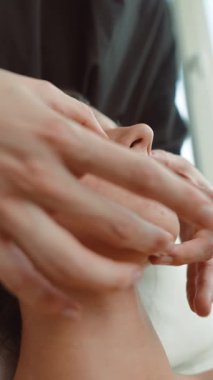 Yüz masajı estetisyeninin elleri çene hattına masaj yapıyor, müşteri yatakta gevşiyor, sivilce dokusu görünür, yumuşak doğal ışık