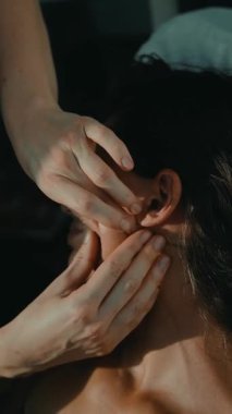 Kafatası osteopati seansına katılan beyaz kadın, pratisyen kulak ve çene manipüle etmek için parmak uçları kullanır, yumuşak klinik