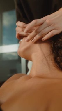 Yakın plan beyaz kadın yüz masajı yaptırıyor estetisyen eller çene ve boyun boyunca süzülüyor, sıcak gün ışığı, çıplak omuzlar.,