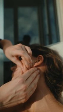 Siluet beyaz kadın, masajcı tarafından boyun ve kulak boşaltılıyor. Pratisyen, akşam penceresi ışığı ve yumuşak gölgeler, eller tarafından.