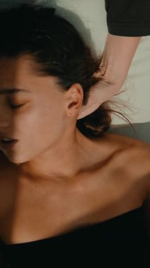 Yatan kadın hafifçe gülümserken sağlık koçu nazikçe boyun terapisi uygular parmaklarını sallar kulak ve çene hizasına, güneş ışığı, sakin ruh hali.