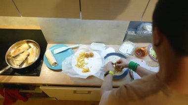 Asyalı bir adam tortilla ambalajına salata katıyor, meze meraklısı doğranmış marul, domates ve kremalı sos ekliyor, organize tezgah.