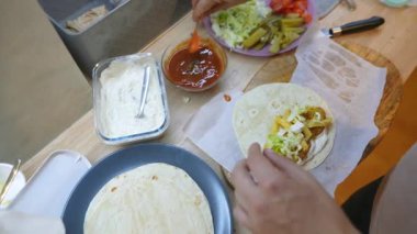 Kapalı eller son sos ve doğranmış sebzeleri tortilla 'ya eklerken parşömen enerjili mutfak sahnesine dikkatlice kaplama yapın.